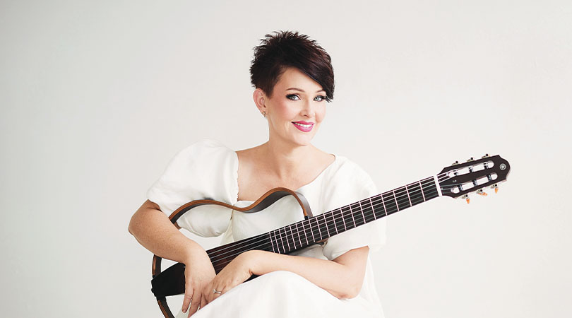 lady with dark short hair wearing white, sitting holding a guitar